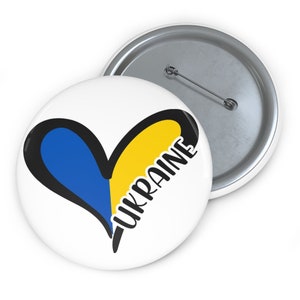 Peut inclure: Un bouton blanc avec un cœur noir rempli des couleurs du drapeau ukrainien, bleu et jaune. Le mot "UKRAINE" est écrit en noir à l'intérieur du cœur.