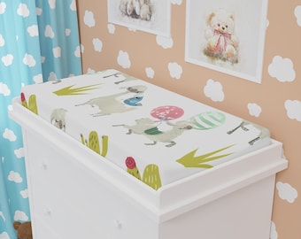 May include: White changing pad cover with a llama and cactus print. The llamas are holding balloons in pink, green and white. The background is white with green cactus plants.