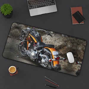 May include: A motorcycle-themed desk mat featuring an orange and black motorcycle with chrome accents. The motorcycle is set against a rocky background. A computer mouse and keyboard are also visible.