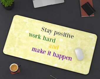 May include: A yellow desk mat with a motivational quote: "Stay positive work hard and make it happen". The quote is in green, yellow, and purple text. A white computer mouse is on the mat.
