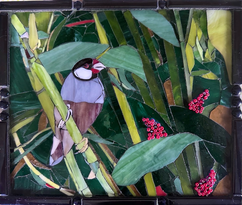 Op de afbeelding: Een moza&iuml;ekkunstwerk met een kleine vogel die op een bamboestok zit. De vogel is grijs en bruin met een rode snavel. De achtergrond is een weelderig groen met rode bessen.