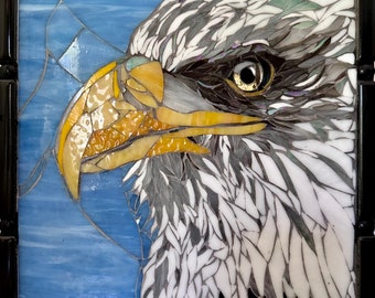 Op de afbeelding: Close-up van een mozaïekkunstwerk dat de kop van een Amerikaanse zeearend toont. Het oog van de adelaar is goudkleurig en de veren zijn een mix van wit, grijs en zwart.