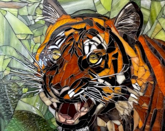 Op de afbeelding: Een close-up van het gezicht van een tijger, gemaakt van kleurrijke glazen mozaïektegels. De bek van de tijger is open, waardoor zijn tanden zichtbaar zijn, en zijn ogen zijn heldergeel. De tijger is geplaatst tegen een achtergrond van groene en bruine mozaïektegels, wat suggereert dat het in een jungle is.
