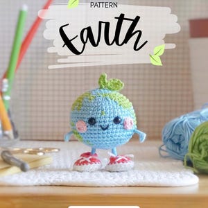 May include: A crocheted Earth amigurumi with a smiling face, blue and green globe, and red and white sneakers. The word "Earth" is written in cursive above the globe. The text "AMIGURUMI PATTERN" is above the word "Earth".