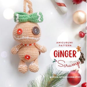 Può includere: Ornamento a forma di omino di pan di zenzero all'uncinetto con fiocco verde, occhi a bottone e dettagli di bottoni rossi. L'ornamento ha un anello per appenderlo e fa parte di un "Amigurumi Pattern" con il testo "Ginger Scrump".