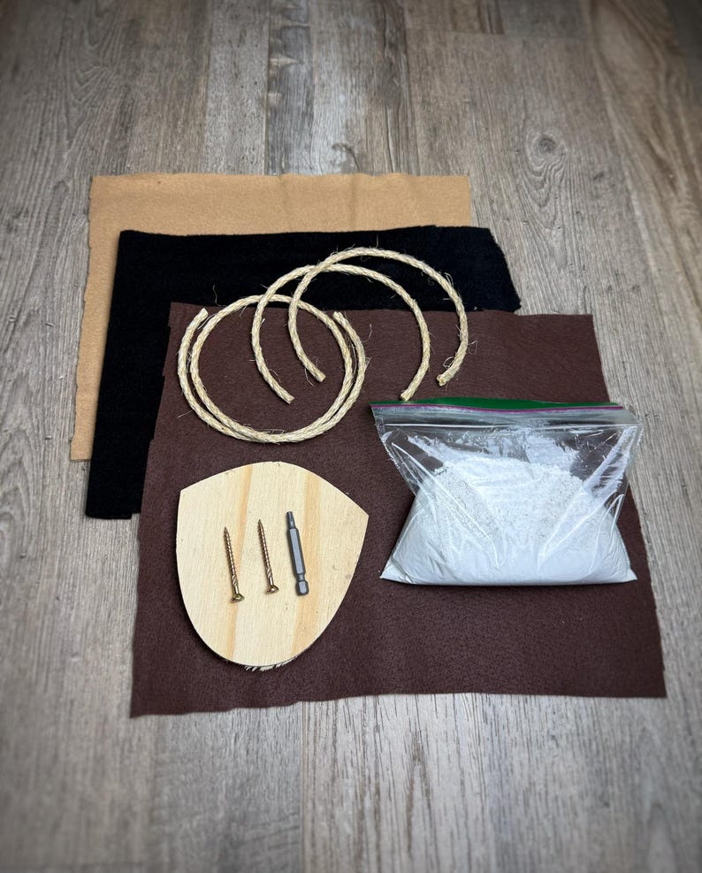 May include: A DIY kit for making a macrame wall hanging. The kit includes a wooden plaque, two pieces of rope, a bag of white powder, two screws, a screwdriver, and three pieces of brown felt.