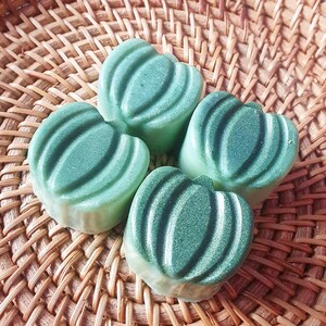 Könnte beinhalten: Vier grüne, herzförmige Seifen mit einer strukturierten Oberfläche. Die Seifen sind in einem Kreis auf einem geflochtenen Korb angeordnet.