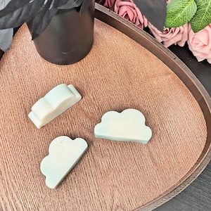 Peut inclure: Trois savons en forme de nuage de couleur bleu clair sur un plateau en bois. Les savons sont disposés en rangée, le plus grand au centre.