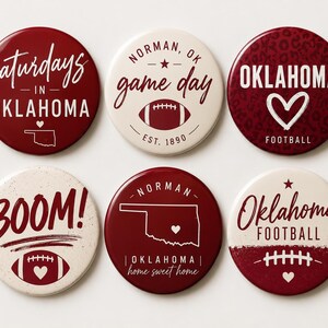 May include: Six circular pinback buttons featuring Oklahoma football themes in maroon and cream. Designs include text like Saturdays in Oklahoma, Norman OK game day, Oklahoma Football, BOOM!, and home sweet home, with graphics of footballs and state maps.