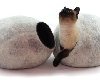 May include: Two gray felt cat beds with a cat peeking out of one of the beds. The cat beds are shaped like a sphere with a round opening.