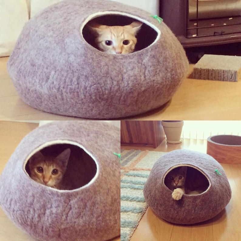May include: Three gray felt cat beds with a round shape and a single opening. A cat is peeking out of the opening of each bed.