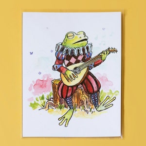 May include: A watercolor illustration of a green frog wearing a red and white jester costume playing a lute on a tree stump. The frog is surrounded by pink and blue watercolor clouds and musical notes.