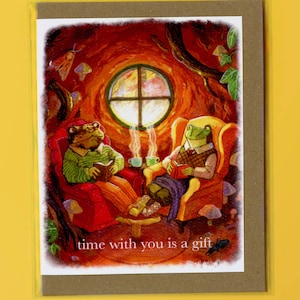 May include: Two frogs sitting in armchairs in a cozy forest setting, reading books and enjoying a cup of tea. The text "time with you is a gift" is written below the image.