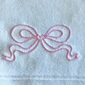 May include: A white fleece blanket with a pink embroidered bow.