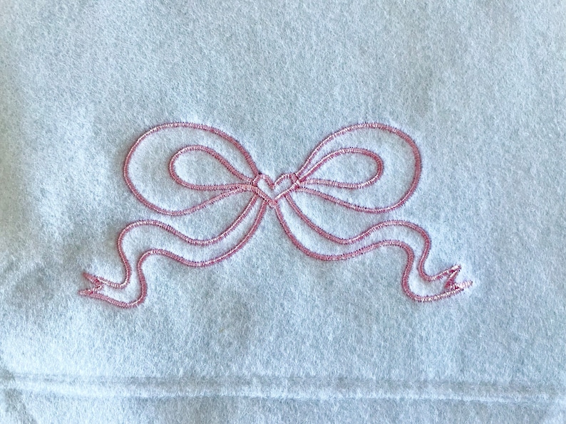 May include: A white fleece blanket with a pink embroidered bow.