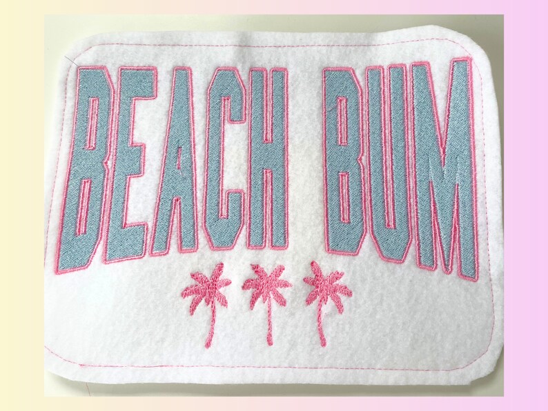 May include: White fabric patch with pink stitching. The patch says "Beach Bum" in blue with a pink outline. There are three pink palm trees below the text.