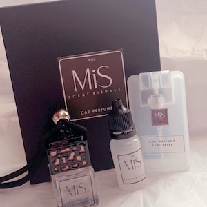 May include: A car fragrance set with a black box, a black and gold hanging diffuser, a clear bottle of fragrance oil, and a clear spray bottle with the text "MiS Scent Rituals Car Perfume 15ml Spray".