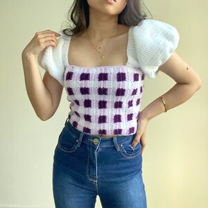 Puede incluir: Un top de crochet blanco con mangas abullonadas y un patr&oacute;n de cuadros vichy morado y blanco.