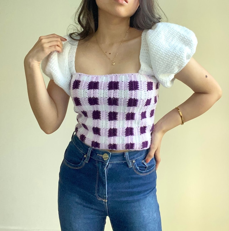 Puede incluir: Un top de crochet blanco con mangas abullonadas y un patr&oacute;n de cuadros vichy morado y blanco.