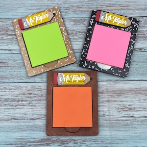 May include: Three wooden notepads with a pencil design and the name "Ms. Taylor" on the pencil. Each notepad has a different colored sticky note: green, pink, and orange.