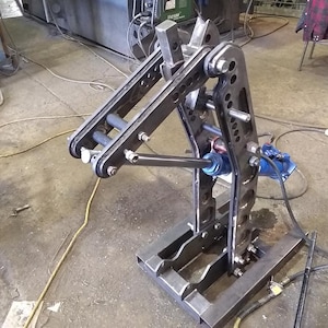 May include: A metal fabrication tool with a blue hydraulic cylinder and a black metal frame. The tool is mounted on a square base with multiple holes. The tool is used to bend metal.