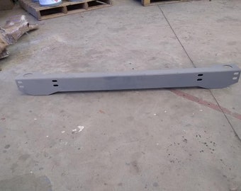 May include: A gray metal bar with holes drilled into it. The bar is lying on a concrete surface.