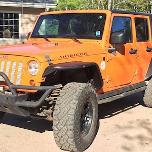 May include: Orange Jeep Wrangler Rubicon with black accents, a black front bumper, and large off-road tyres.