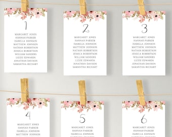 May include: A wooden frame with a white background and a string of clothespins holding cards with floral designs and guest names for a wedding reception. The top card reads "Find your seat" with the names "Hunch & Thany" and the date "05.18.2023".