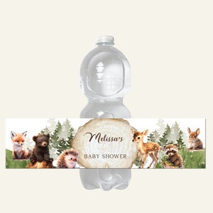 Może przedstawiać: Etykieta na butelkę wody z motywem leśnym. Etykieta zawiera brązowe drewniane koło z tekstem "Baby Shower Melissy" i ilustracje lisa, niedźwiedzia, jeża, jelenia, szop pracza i królika.
