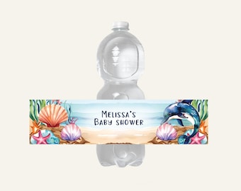 Op de afbeelding: Een waterfles met een decoratief etiket met een strandscène. Het etiket bevat schelpen, zeesterren en een dolfijn. De tekst op het etiket luidt "MELISSA'S BABY SHOWER". Het ontwerp heeft een aquarel stijl met blauwe, roze en oranje tinten.