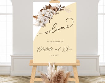 May include: A wedding welcome sign on a wooden easel. The sign is cream-colored with a floral arrangement and the word "welcome" in cursive. The names "Charlotte and Steve" and the date "9.26.2023" are also displayed.