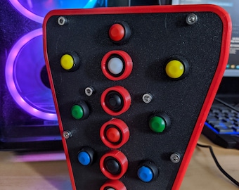 May include: A black and red gaming controller with multiple buttons, including red, yellow, green, blue, and white buttons. The controller is mounted on a black base.