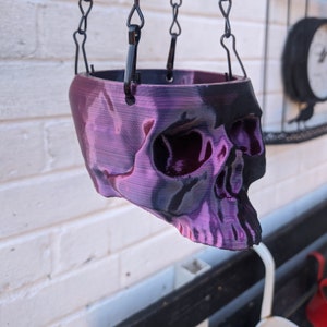 May include: A purple and black skull-shaped hanging planter with a black metal chain.