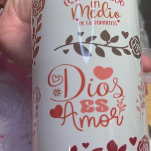 May include: White ceramic mug with a yellow lid. The mug features a floral design with red and brown leaves and hearts. The text on the mug reads "Dios esta conmigo en medio de la tormenta" and "Dios es amor".