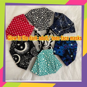 May include: Six glow-in-the-dark face masks with different celestial patterns. The masks are made of fabric and have elastic ear loops. The patterns include stars, moons, and constellations. "Glow in the dark adult/teen face masks" is written on the white background.