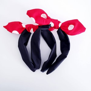 May include: Two black fabric headbands with red and white polka dot bows. The bows are tied in a knot and the ends are left loose.