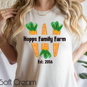 May include: White t-shirt featuring a graphic of three orange carrots with green tops. The text "Hopps Family Farm Est: 2016" is printed on the shirt.