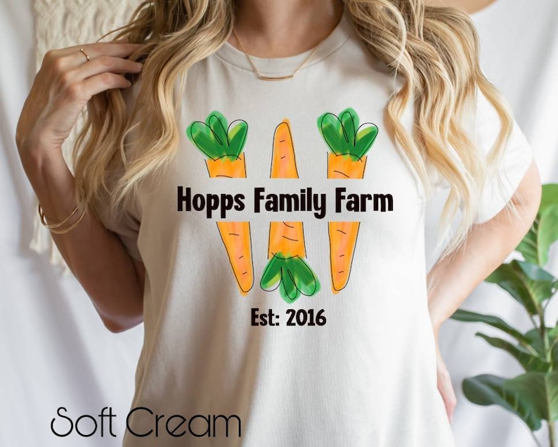 May include: White t-shirt featuring a graphic of three orange carrots with green tops. The text "Hopps Family Farm Est: 2016" is printed on the shirt.