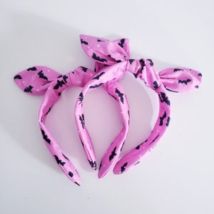 May include: Two pink headbands with a black bat print. The headbands are tied in a bow at the top.