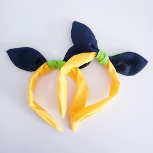 Può includere: Due fasce fatte a mano con una fascia gialla e accenti a forma di foglia blu navy. Le fasce sono collegate con un tessuto verde. Queste fasce sono un accessorio elegante per ogni occasione.