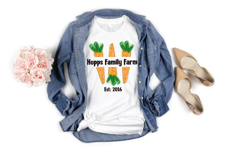 May include: White t-shirt featuring a design of three carrots and the text "Hopps Family Farm Est: 2016".