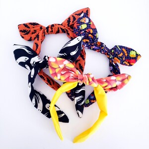 May include: Three Halloween-themed headbands with different patterns. One headband has a black and white ghost pattern, another has an orange and black bat pattern, and the third has a colorful candy corn pattern.