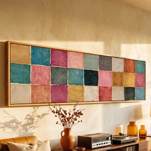 Puede incluir: Una pieza de arte mural rectangular y alargada que presenta una cuadrícula de veinticuatro cuadrados en varios colores, incluyendo verde azulado, rosa, amarillo, negro y gris. La obra está enmarcada en madera clara y tiene textura.