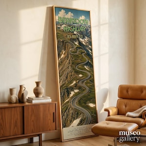 May include: A tall, vertical framed wall art print featuring a winding mountain road. The text reads Beartooth Highway U.S. Route 212. The image depicts a high-altitude landscape with green slopes, rocky terrain, and patches of snow under a blue sky.