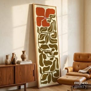 May include: A tall, rectangular framed wall art piece featuring a stylized illustration of a large, burnt-orange flower with a small pink center, set against a cream background with long, winding dark olive green stems and leaves.