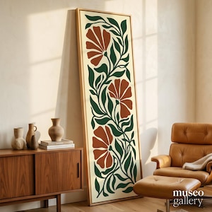 May include: A tall, rectangular framed wall art piece featuring a vertical botanical illustration with three large, rust-colored stylized flowers connected by dark green flowing leaves and stems on a cream-colored background.