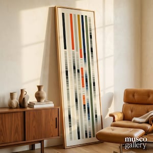 May include: A tall, rectangular framed wall art piece featuring a vertical pattern of thin, multicolored stripes in shades of orange, blue, green, black, and cream. The artwork is encased in a light-toned wooden frame and stands upright.