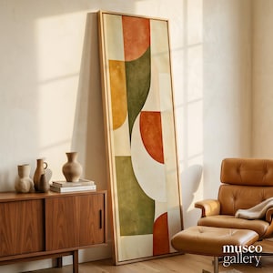 May include: A tall, rectangular framed wall art piece featuring an abstract composition of geometric shapes in muted tones of terracotta, olive green, mustard yellow, and cream, set within a light-colored wooden frame leaning against a wall.
