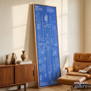 May include: A tall, rectangular framed wall art piece featuring a blue and white technical blueprint of an Atlas V rocket. The print displays detailed schematic diagrams, component labels, and technical text, all encased in a light wood frame.