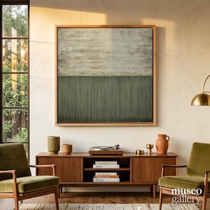 Puede incluir: Una pintura abstracta cuadrada en un marco de madera clara que presenta una sección superior beige texturizada y una sección inferior verde oliva oscuro con líneas verticales. La obra se exhibe sobre un mueble multimedia de madera.